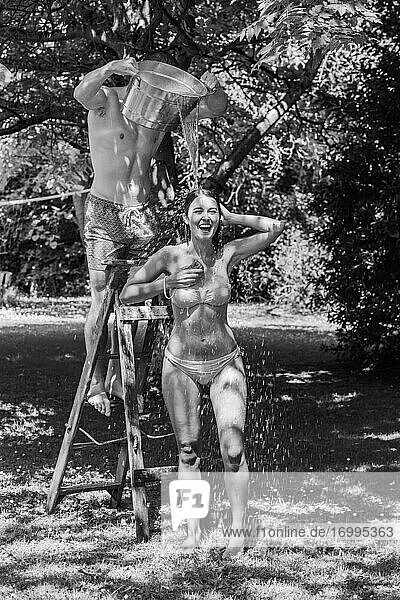 Playful junger Mann gießt Wasser über Freundin im Bikini im Sommer Hinterhof