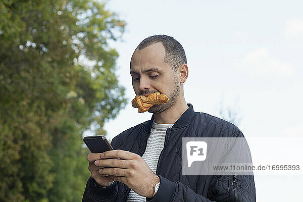Junger Mann beim Essen und mit Smartphone