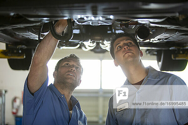 Two mechanics work on the underside of a care on a lift in a repair shop