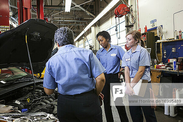 Drei Mechanikerinnen unterhalten sich und sehen sich den Motor eines Autos in einer Reparaturwerkstatt an