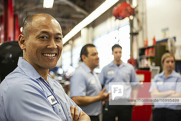 Porträt eines lächelnden pazifischen Inselbewohners  der eine Werkstatt betreibt  mit einem Team im Hintergrund