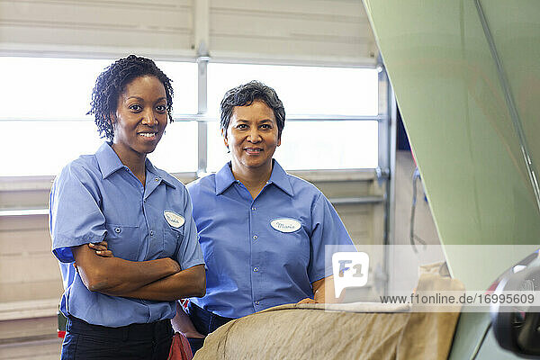 Porträt von zwei lächelnden Mechanikerinnen in einer Autowerkstatt.