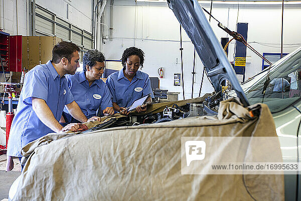 Drei Mechaniker teilen sich ein digitales Tablet und planen die Arbeit an einem Auto  das zur Reparatur ansteht