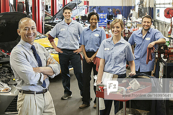 Portrait of smiling auto repair shop team with Pacific Islander owner
