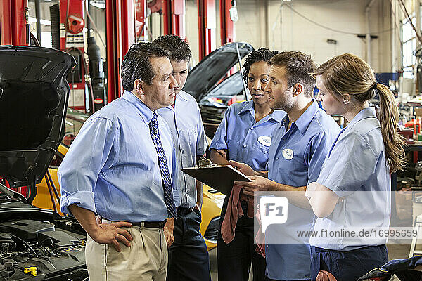 Team of mechanics working on a car discuss a problem in an auto repair shop