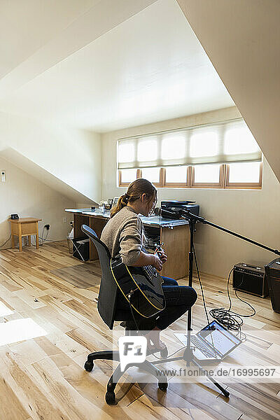 Vierzehnjähriges Teenager-Mädchen spielt Gitarre und singt zu Hause auf dem Dachboden