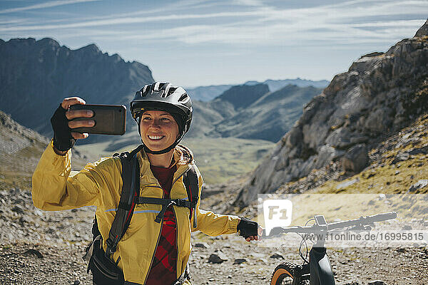 Lächelnde Radfahrerin  die ein Selfie mit ihrem Mountainbike am Berg macht  Nationalpark Picos de Europa  Kantabrien  Spanien