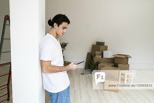 Junger Mann benutzt ein Mobiltelefon  während er an einer Säule in einem neuen Haus steht