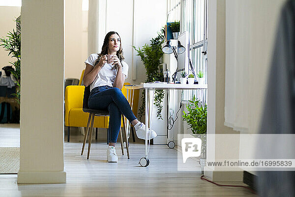 Young businesswoman holding coffee cup looking away at office