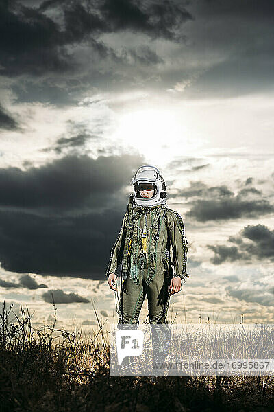 Mann posiert als Astronaut verkleidet auf einer Wiese mit dramatischen Wolken im Hintergrund