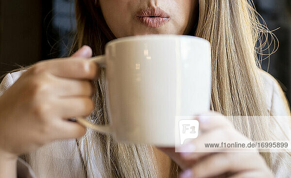 Frau bläst Kaffee und hält Kaffeetasse im Café