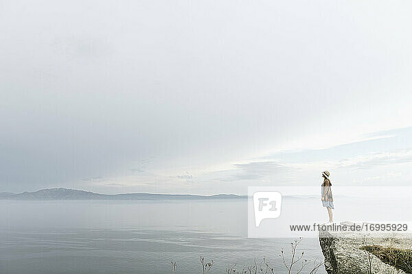 Frau steht auf einem Felsen und blickt auf das Meer