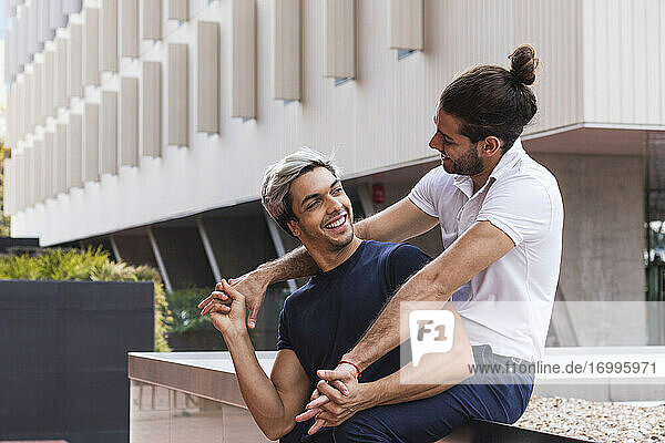 Lächelnder Mann  der seinen schwulen Partner ansieht  während er an einem Gebäude in der Stadt sitzt