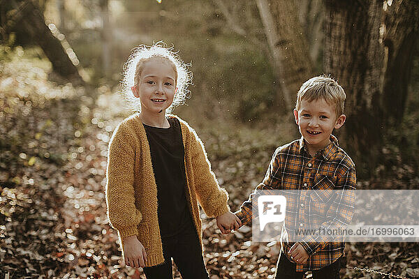Bruder und Schwester lächelnd und händchenhaltend im Wald stehend