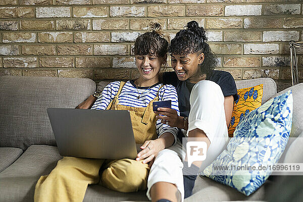 Smiling lesbian couple doing online shopping while sitting at home