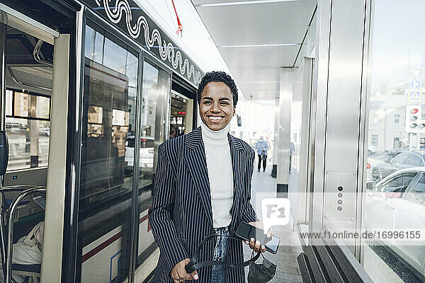 Glückliche Geschäftsfrau mit Mobiltelefon an der Bushaltestelle während des COVID-19-Ausbruchs