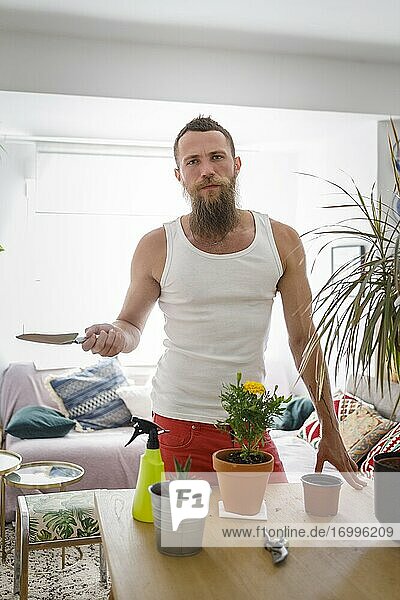Male hipster holding shovel standing by table at home