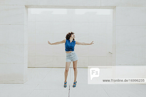 Carefree mid adult woman with arms outstretched standing against tiled wall