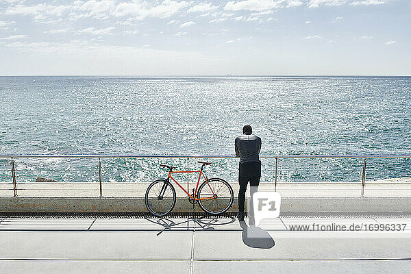 Rückansicht eines Mannes mit Fahrrad auf der Uferpromenade