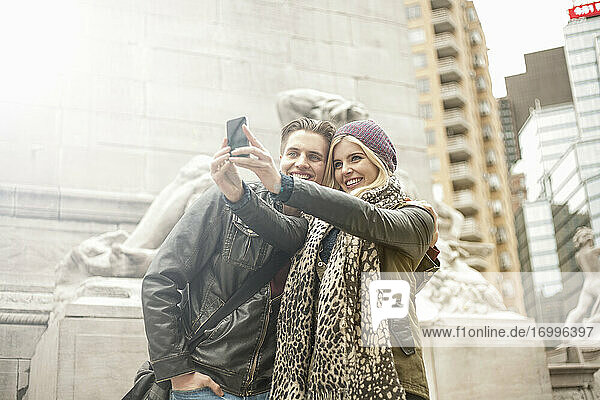 Junge Frau nimmt Selfie mit Mann durch Handy  während in der Stadt stehen