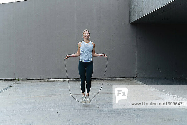 Young sportswoman skipping rope while standing against wall