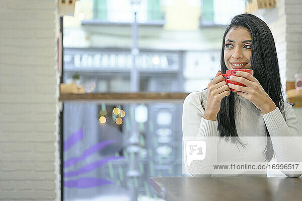 Nachdenkliche Unternehmerin schaut weg  während sie eine Kaffeetasse im Café hält