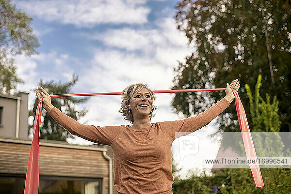 Lächelnde Frau  die ein Fitnessband hält  während sie im Hinterhof steht