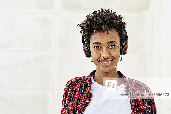 Lächelnde junge Afro-Frau hört Musik an einer weißen Wand