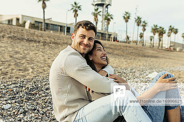 Junges Paar lacht  während sie sich am Strand umarmen
