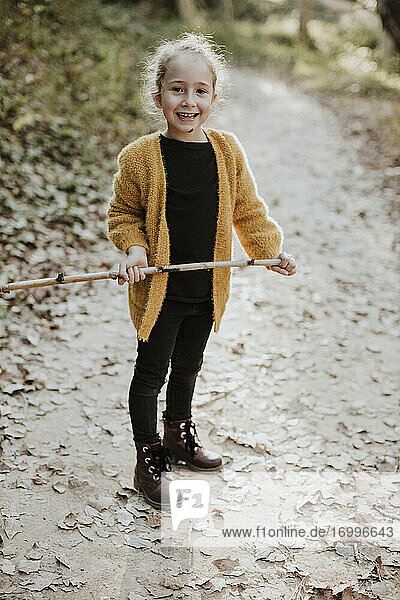 Smiling girl playing with stick while standing on footpath in forest