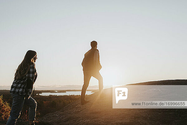 Junges Paar geht gegen die untergehende Sonne einen Hügel hinauf