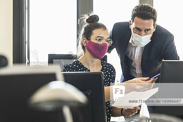 Geschäftsleute mit Gesichtsmaske diskutieren bei der Arbeit im Büro