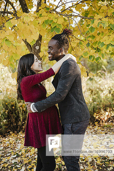 Lächelndes multiethnisches Paar umarmt sich im Herbst im Park