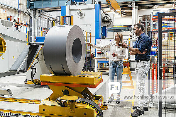 Eine Unternehmerin prüft eine Stahlwalze mit einem männlichen Kollegen  während sie in einer Fabrik stehen