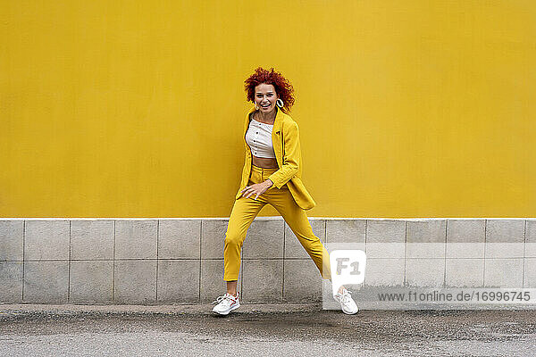Energetische junge Frau in gelbem Anzug läuft und springt vor einer gelben Wand