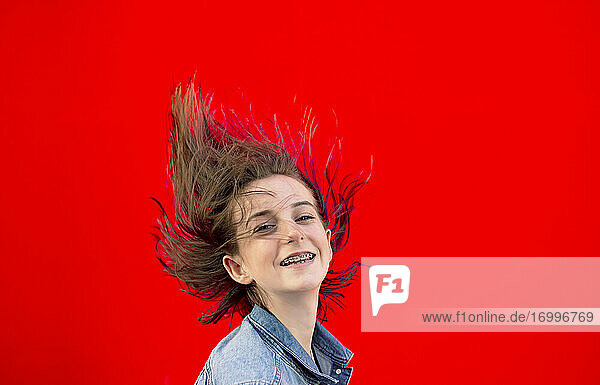 Porträt eines lächelnden Teenagers mit Zahnspange und wehendem Haar vor rotem Hintergrund