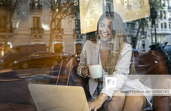 Lächelnde Frau  die einen Laptop benutzt  während sie in einem Café Kaffee trinkt