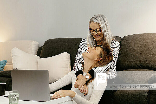 Happy mother with arm around on daughter sitting at home