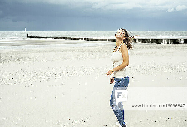 Lächelnde Frau steht mit geschlossenen Augen am Strand