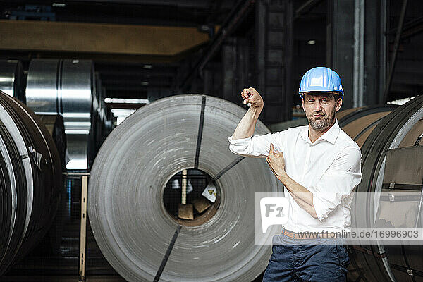 Businessman pointing at flexing muscle while standing in factory