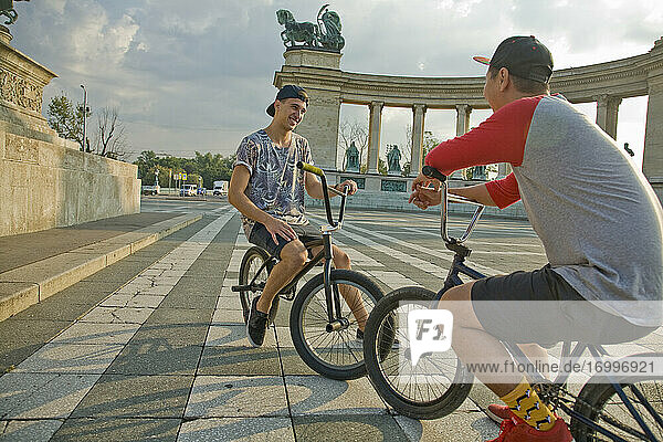 Young male BMX bikers taking break while sitting on bicycles at Hero's Square  Budapest  Hungary