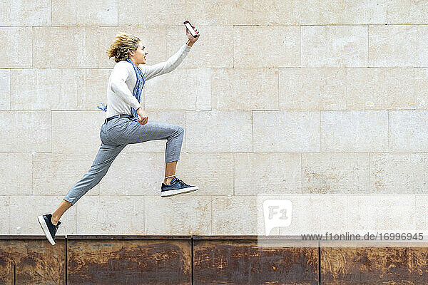 Junger Mann  der ein Selfie mit seinem Mobiltelefon macht  während er gegen eine Wand läuft