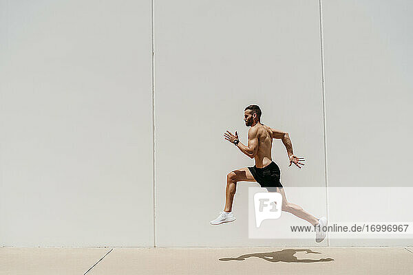 Barechested male athlete jumping at a wall