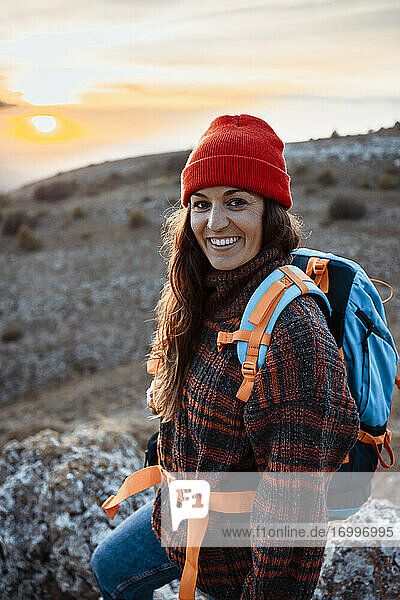 Glückliche Wanderin mit Rucksack auf einem Berg stehend bei Sonnenuntergang