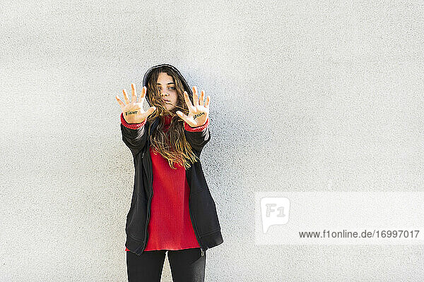Portrait of serious teenage girl showing the words fight and sexism written on her palms
