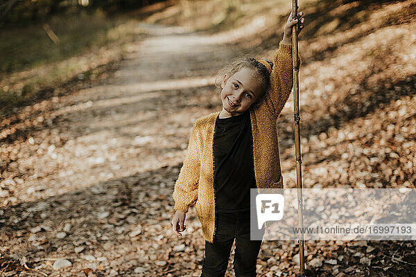 Mädchen lächelt und hält einen Stock auf einem Waldweg