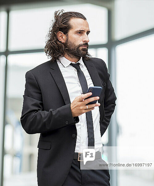 Porträt eines bärtigen Geschäftsmannes  der mit einem Smartphone in der Hand in einem Haus steht