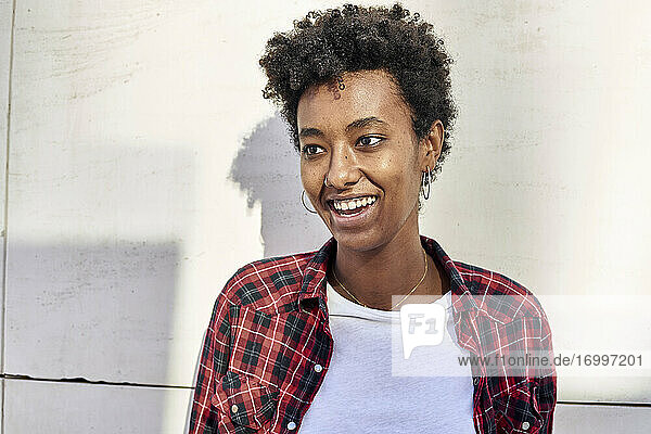 Smiling young Afro woman looking away against white wall