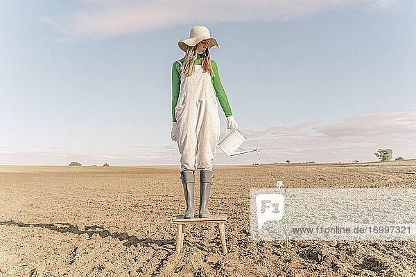 Woamn standing on stool  watering flower on barren field