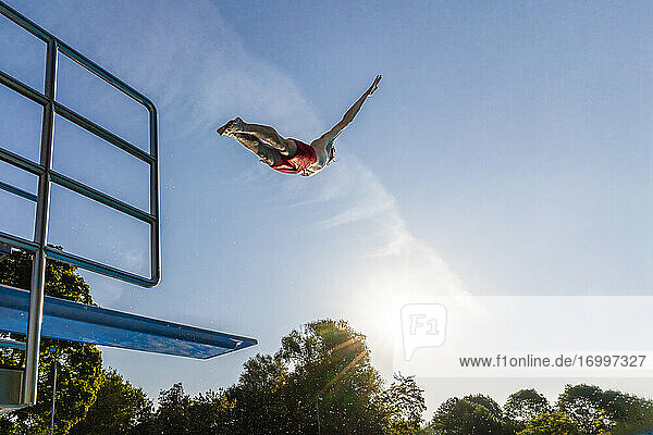 Young man jumping from diving board against blue sky on sunny day